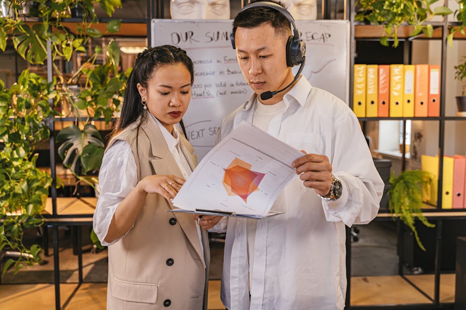 Two business professionals analyze reports in an office with green decor. Collaborative work environment.